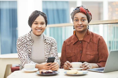 Free Two women sitting together with coffee and snacks, smiling and relaxed indoors. Stock Photo