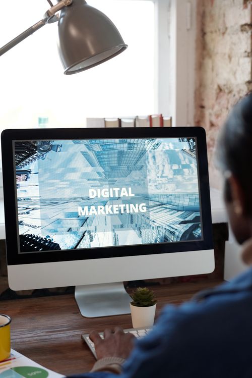 Free An individual focused on digital marketing on a desktop computer in a cozy workspace. Stock Photo