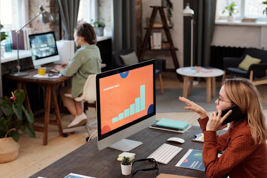 Two business professionals engaged in work with computers and phone in a modern office setting.