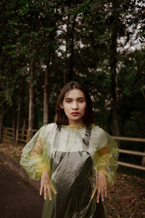Serious woman in raincoat standing on roadside against trees