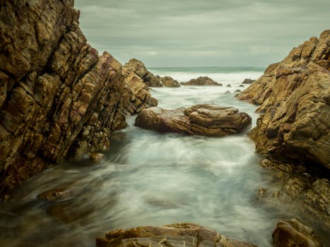 Tranquil seascape with rocky shoreline, gentle waves, and muted sunset colors.