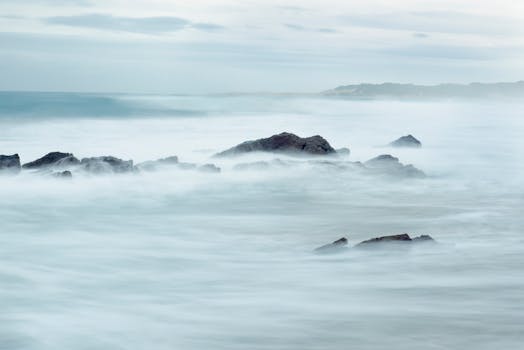 A tranquil seascape showcasing misty waves washing over coastal rocks at dawn, creating a dreamy atmosphere.