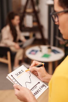 A man drawing a business strategy graph in a notebook indoors.