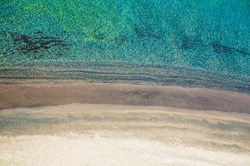 Drone view of empty sandy beach washed by clean water of peaceful ocean in daytime