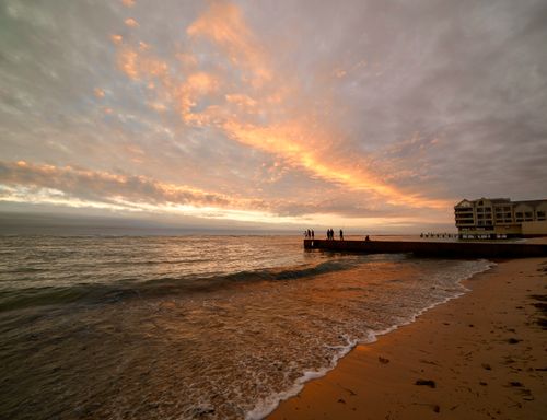 Free A serene sunset over a sandy beach with people silhouetted on a pier. Stock Photo