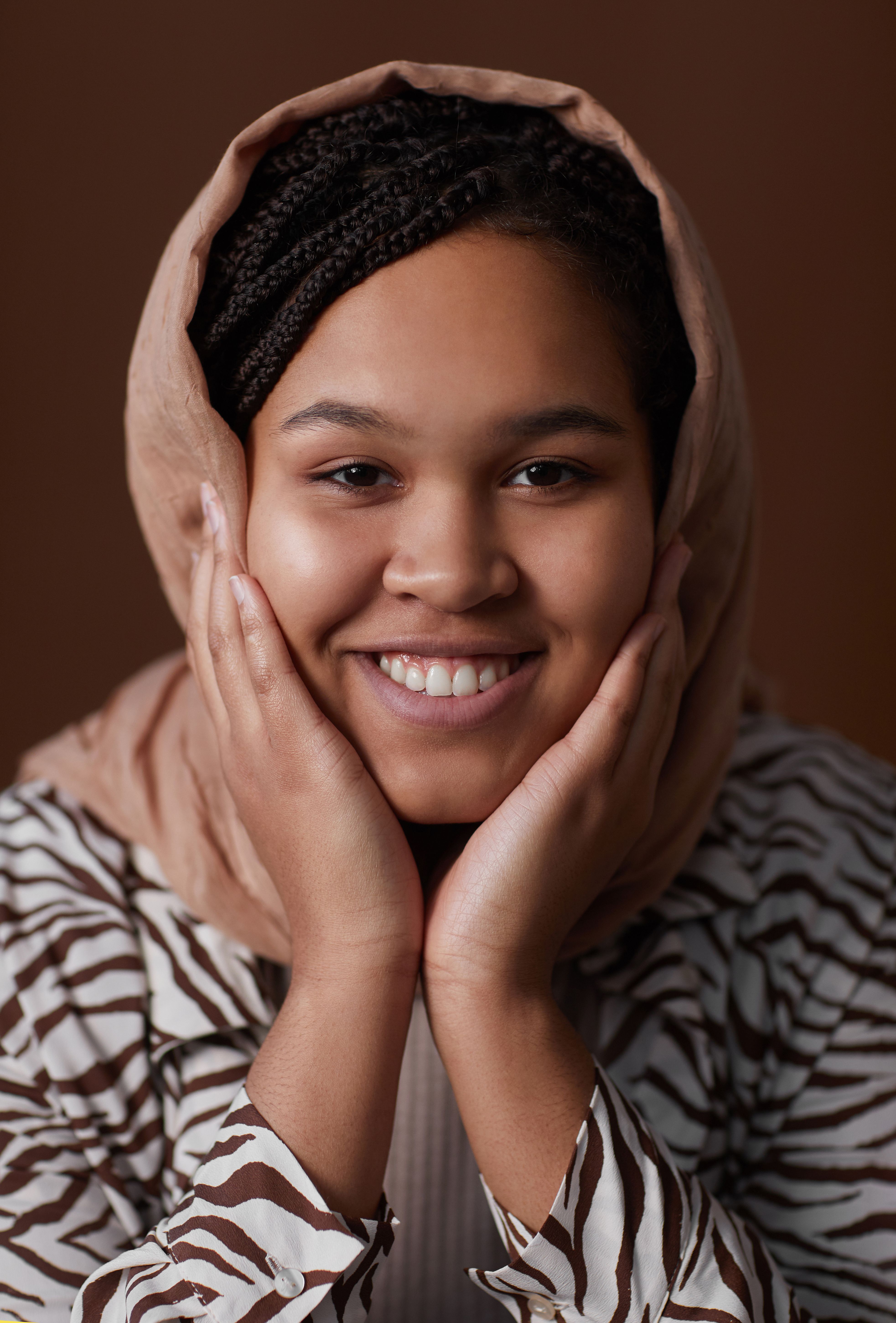 Elegant portrait of a woman with hijab, hands on chin, exudes confidence and joy.