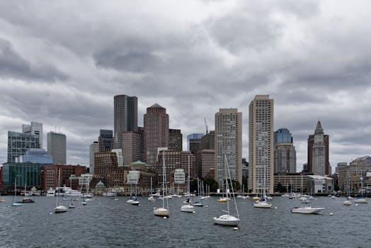 Boston's iconic skyline with boats in the harbor under a dramatic cloudy sky.