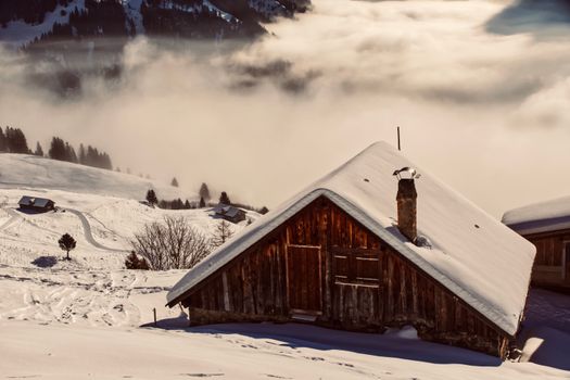 Timber house on snowy mountain slope with mist in lowland