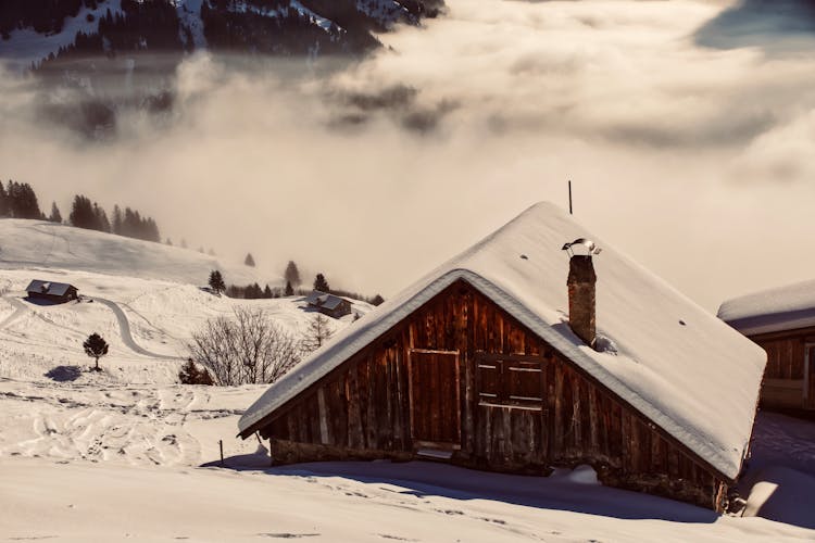 Timber House On Snowy Mountain Slope With Mist In Lowland