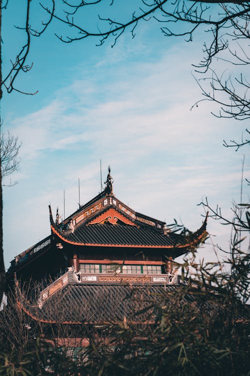 From below of traditional oriental temple with ornamental roof in garden against cloudy blue sky