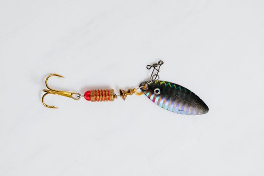 A close-up shot of a colorful metallic fishing lure with hook on a white surface.