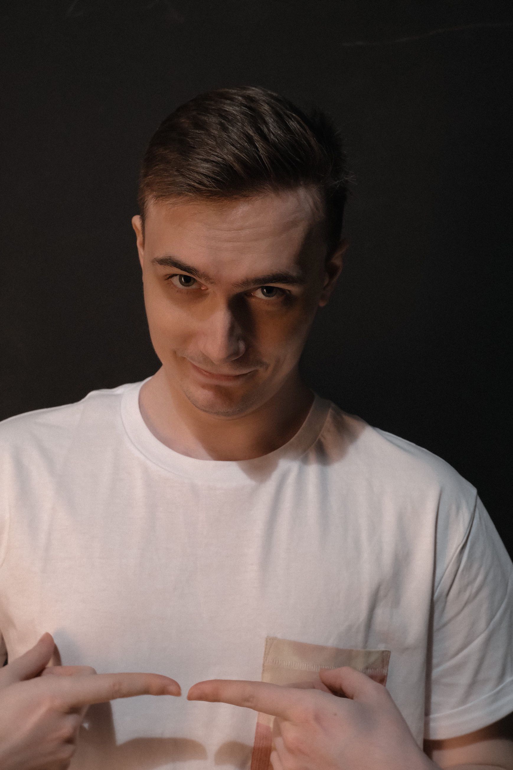 Portrait of a confident young man in a white t-shirt against a dark background.