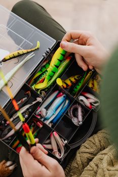 Bright fishing lures and equipment in an organized tackle box being handled.