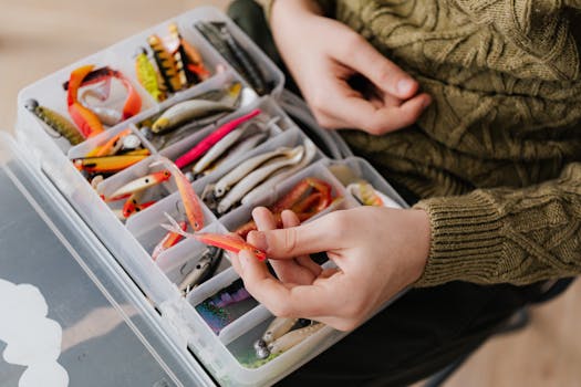 Hand selecting fishing lure from organized plastic container filled with assorted bait.
