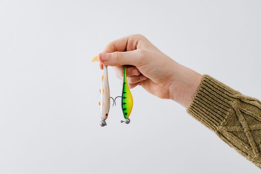 A close-up of a hand holding two colorful fishing lures against a white backdrop.