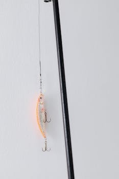 Close-up of a fishing lure hanging on a line against a white wall, showcasing detailed hooks and colors.