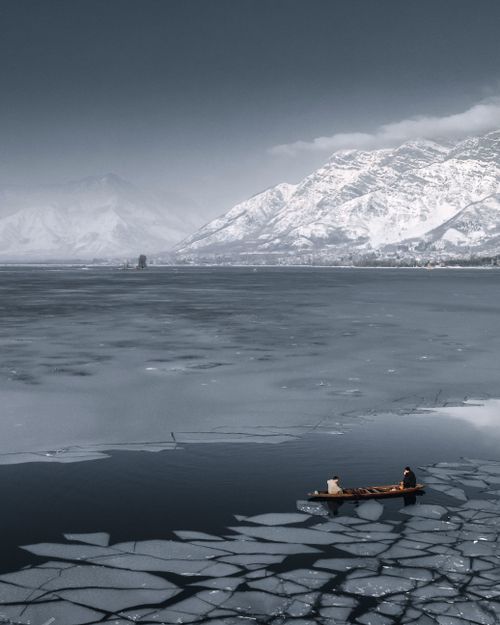 Free A wooden boat navigates a frozen lake with snowy mountains in Srinagar. Stock Photo