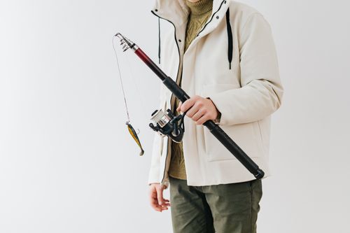 Free Person in a white jacket holding a fishing rod with lure against a neutral background. Stock Photo