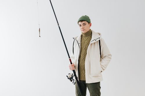 Free Young man in knitwear studio shoot holding a fishing rod, expressing hobby and style. Stock Photo