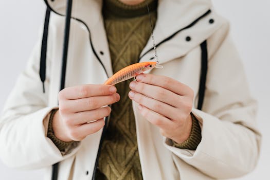 Close-up of hands holding a vibrant orange fishing lure in winter attire.