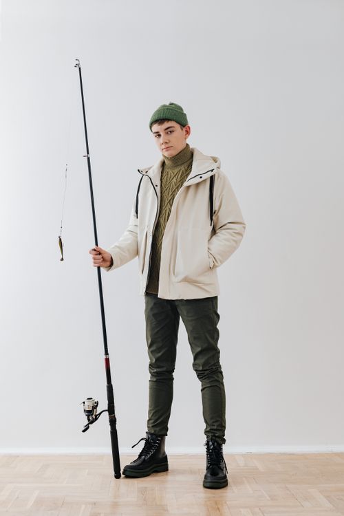 Free Portrait of a young man holding a fishing rod, wearing a beanie and white jacket indoors. Stock Photo