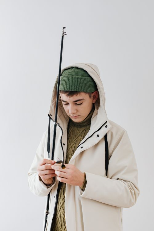 Free A young man holding a fishing rod while wearing a white jacket and green beanie indoors. Stock Photo