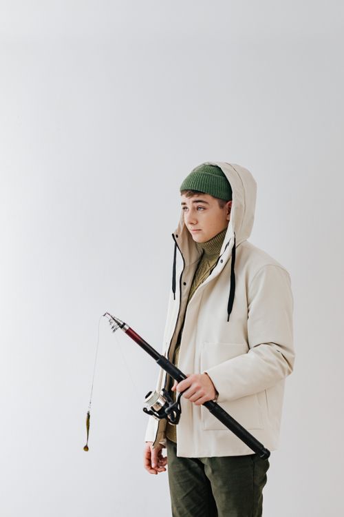 Free Portrait of a young man in winter fashion holding a fishing rod against a white background. Stock Photo