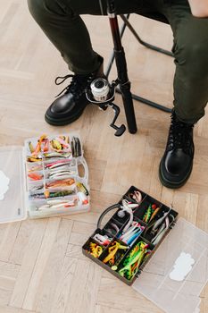Top view of organized fishing gear and lures next to seated person indoors.
