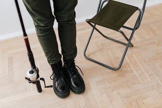 Close-up of a person in black boots holding a fishing rod next to a folding chair.