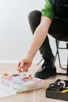 A fisherman organizing colorful lures in a plastic container indoors.