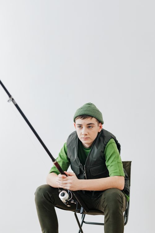 Free Teenage boy sitting indoors holding fishing rod, showing interest in fishing hobby. Stock Photo