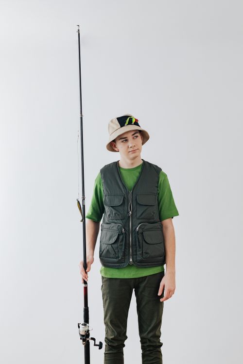 Free Teenage boy in green outfit with fishing rod, posing indoors. Stock Photo