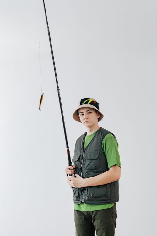 Free Teenager holding a fishing rod, dressed in a bucket hat and vest, ready for fishing outdoors. Stock Photo