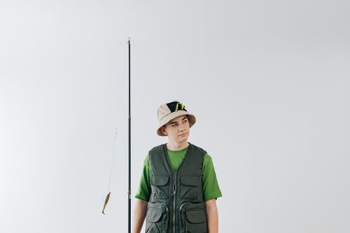 Free Teen boy posing with fishing rod and gear against a plain backdrop, showcasing leisure and fishing lifestyle. Stock Photo
