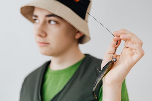 Free A focused teenager in a bucket hat holds a fishing lure, showcasing a hobbyist's interest. Stock Photo