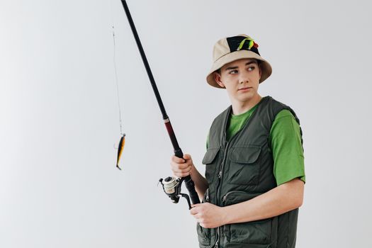 Teenage boy wearing a fishing vest and holding a rod, ready for fishing adventure indoors.