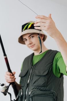 Young male in a bucket hat displaying a fishing lure with a fishing rod in hand.