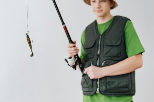 Free Teen boy in a bucket hat holding a fishing rod with a lure, showcasing a fishing hobby. Stock Photo