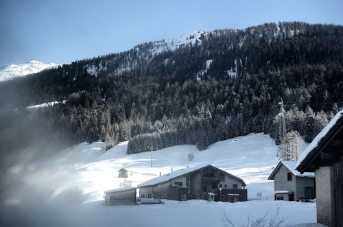 Free Snow-covered Swiss village with mountain backdrop and coniferous trees in winter. Stock Photo