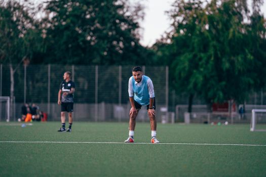 Male soccer player in uniform standing in field and leaning on hands during training in grassy field
