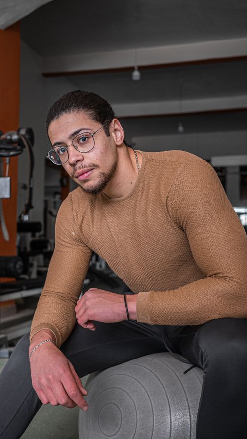 Free Young man with eyeglasses sitting on stability ball in gym, showcasing fitness and style. Stock Photo