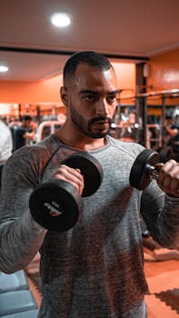 A muscular man intently lifting dumbbells in a gym setting, showcasing strength and fitness.