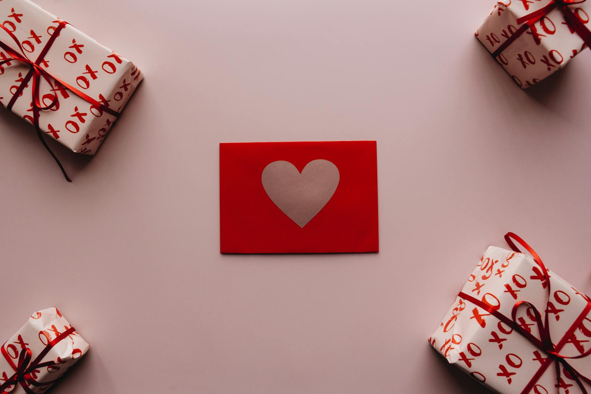 Red envelope with heart design surrounded by gift boxes wrapped in XO paper, perfect for romantic occasions.