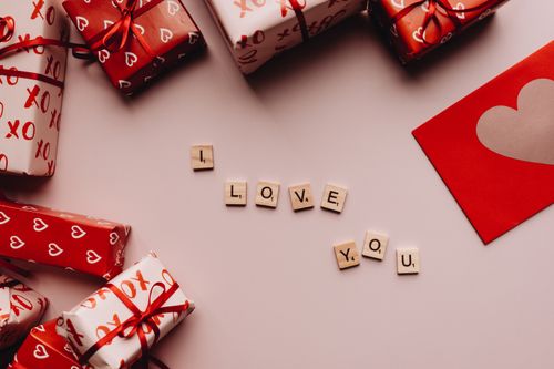 Free Valentine's Day gifts with heart-patterned wrapping paper and 'I Love You' spelled with Scrabble tiles. Stock Photo