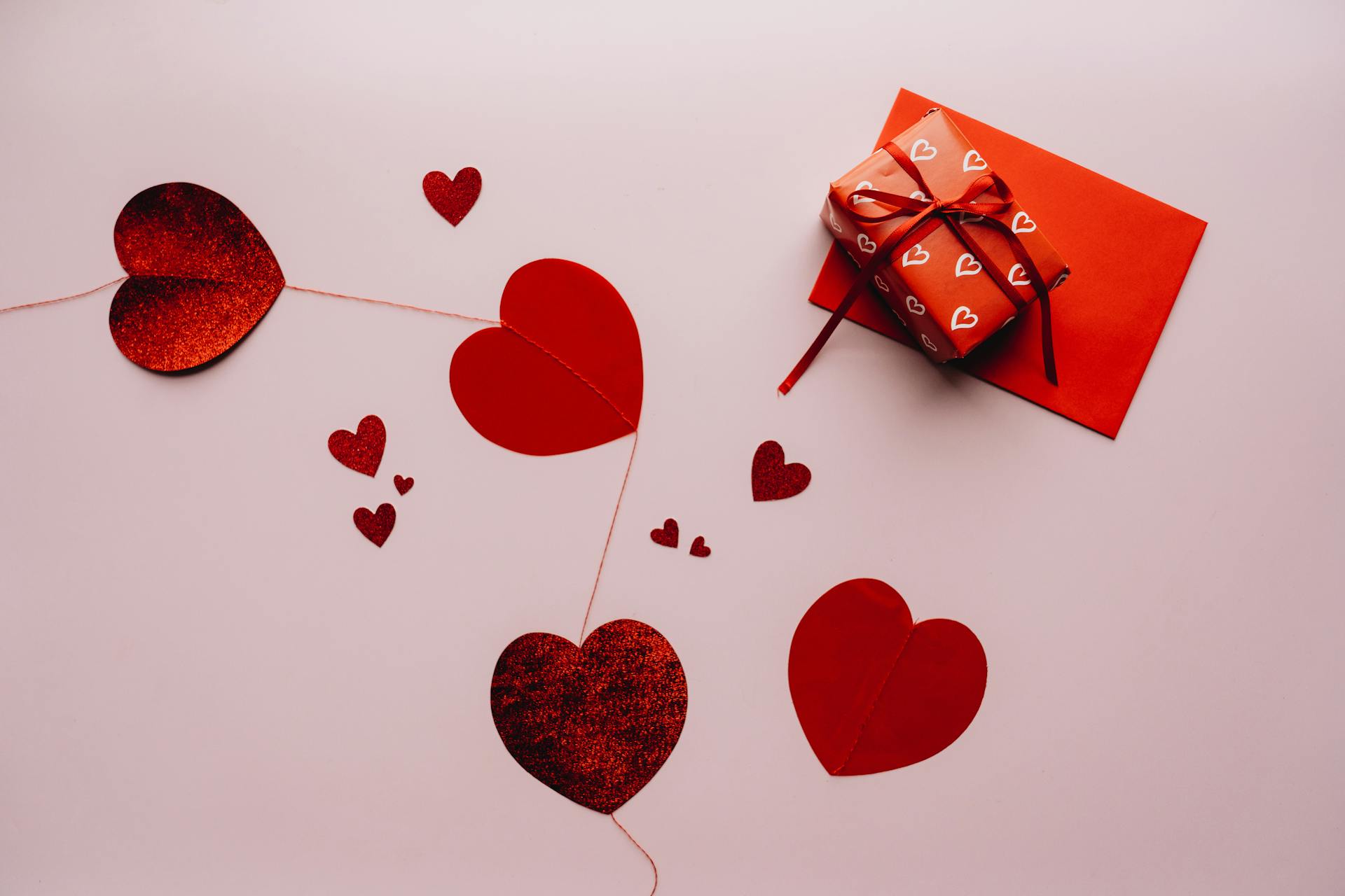 Celebrate love with a gift wrapped in heart-pattern paper, accompanied by red hearts and an envelope.