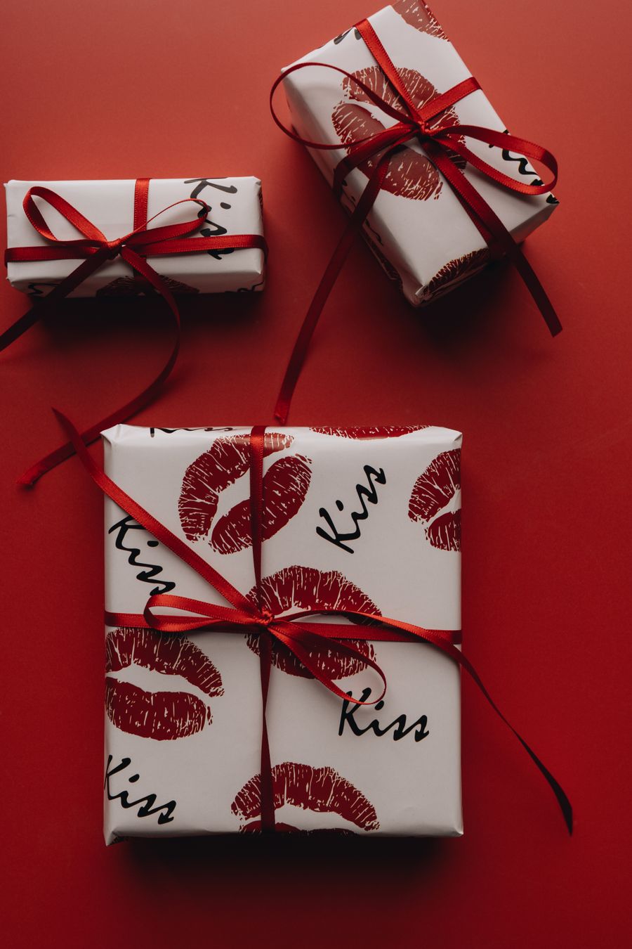 Stylishly wrapped gifts featuring a playful kiss motif on a vibrant red background.