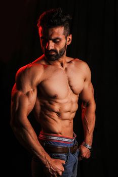 Shirtless muscular man posing in studio with dramatic lighting, showcasing fitness and physique.