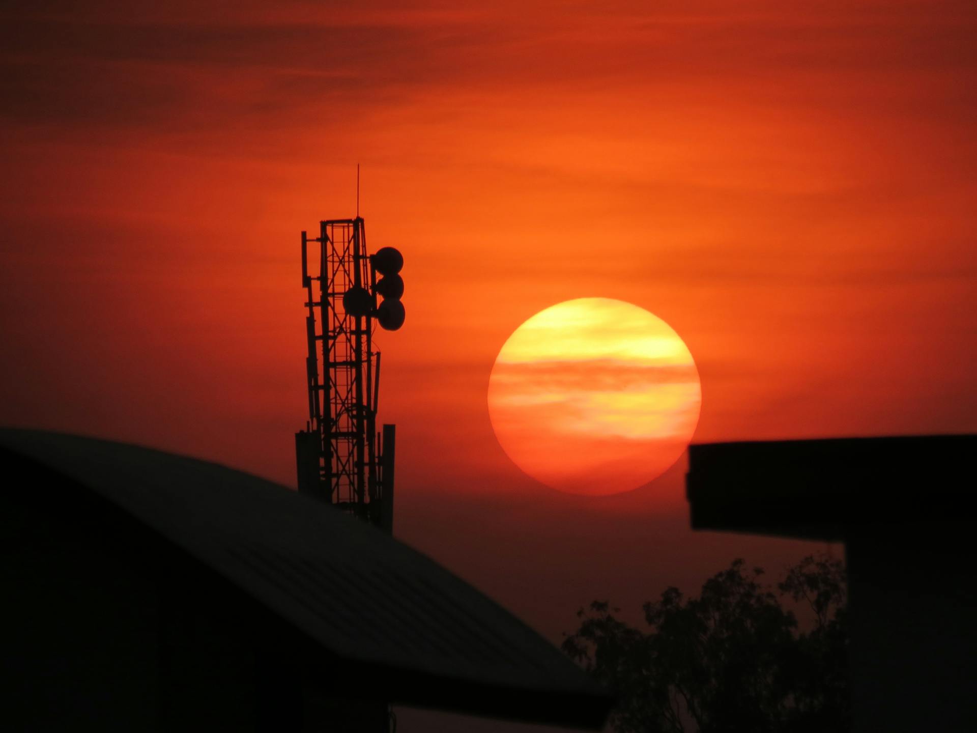 Striking silhouette of a communication tower at sunset with a vibrant orange sky.