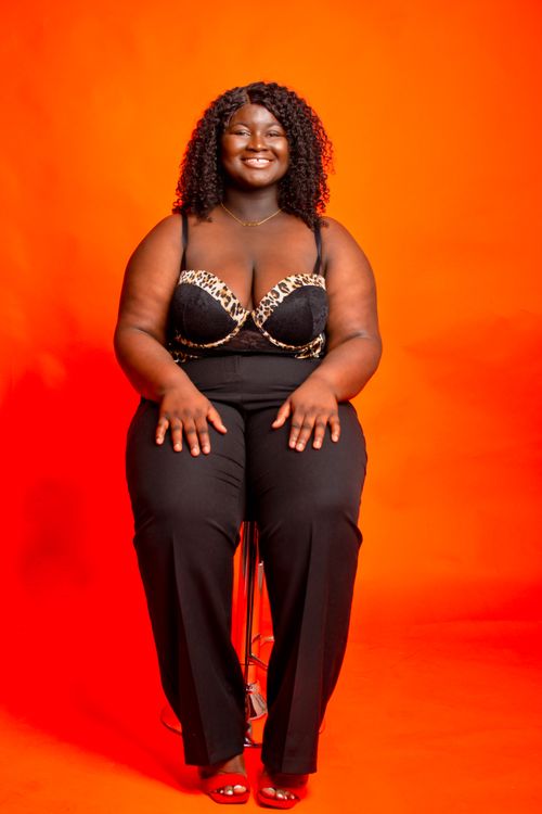 Free Confident plus-size model with curly hair in fashionable attire against an orange background. Stock Photo