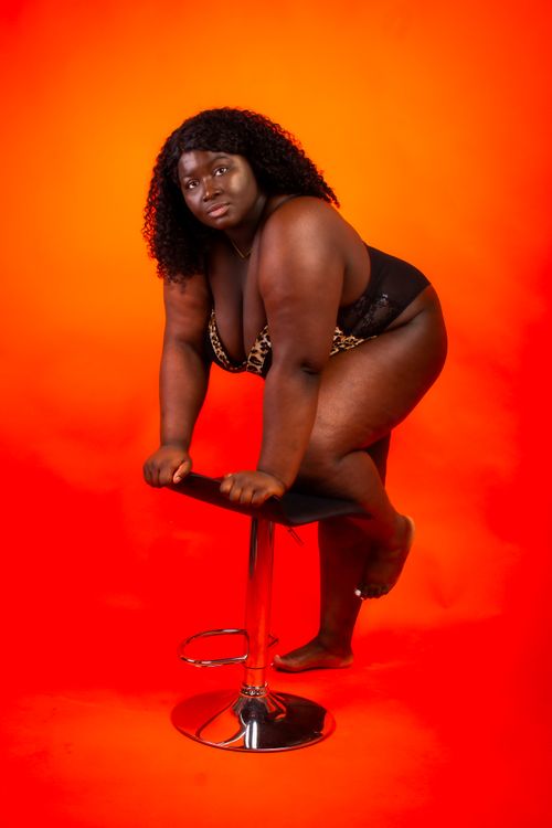 Free Studio portrait of a confident woman posing on a bar stool against an orange backdrop. Stock Photo